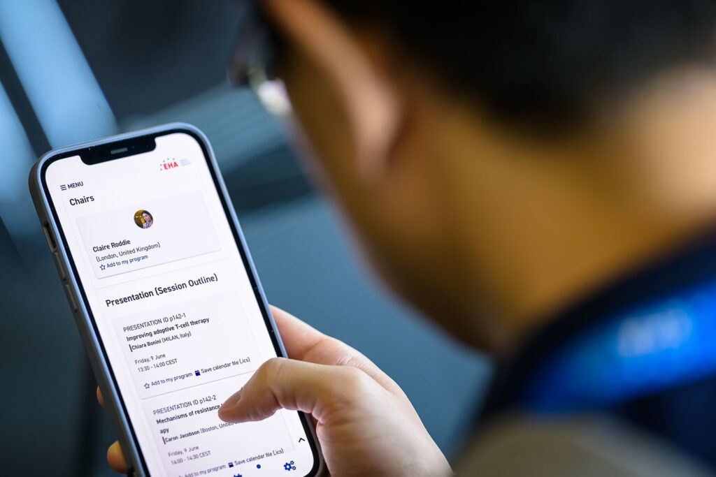 A close-up shot of a person looking at the EHA2023 app on a smartphone.