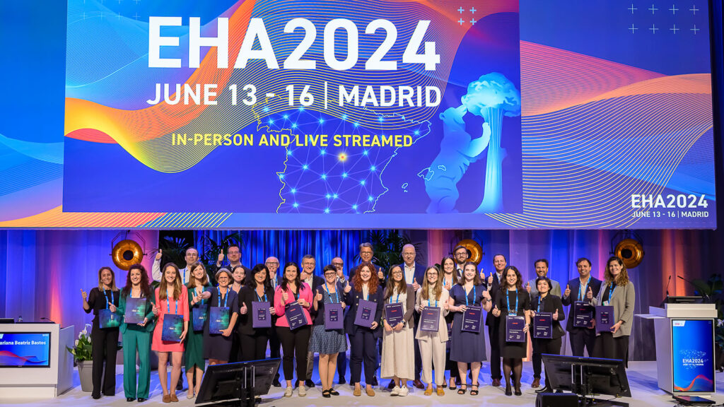 EHA2024 award winners on stage. There are around 20 winners in total, and almost all of them are giving a 'thumbs up' sign.
