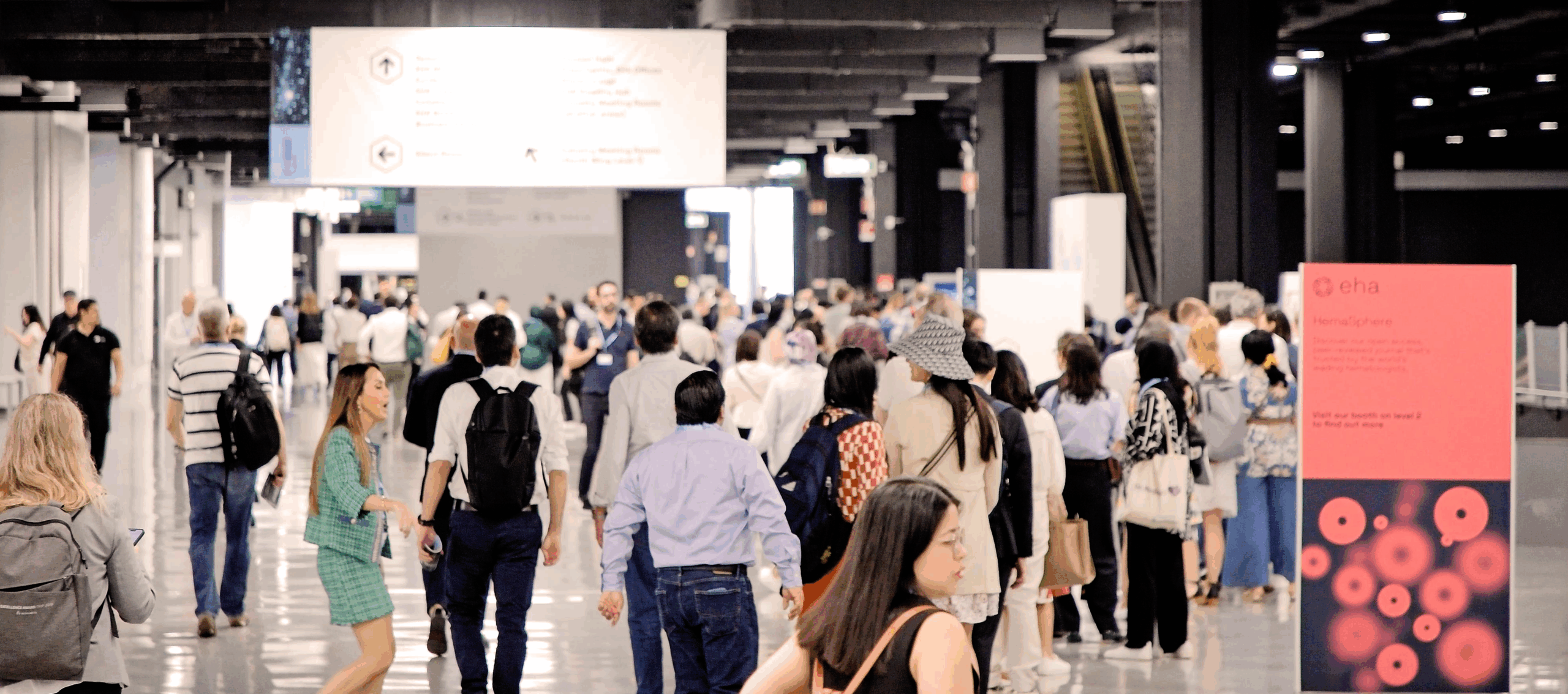 Dozens of delegates in an large, open corridor at EHA2025.