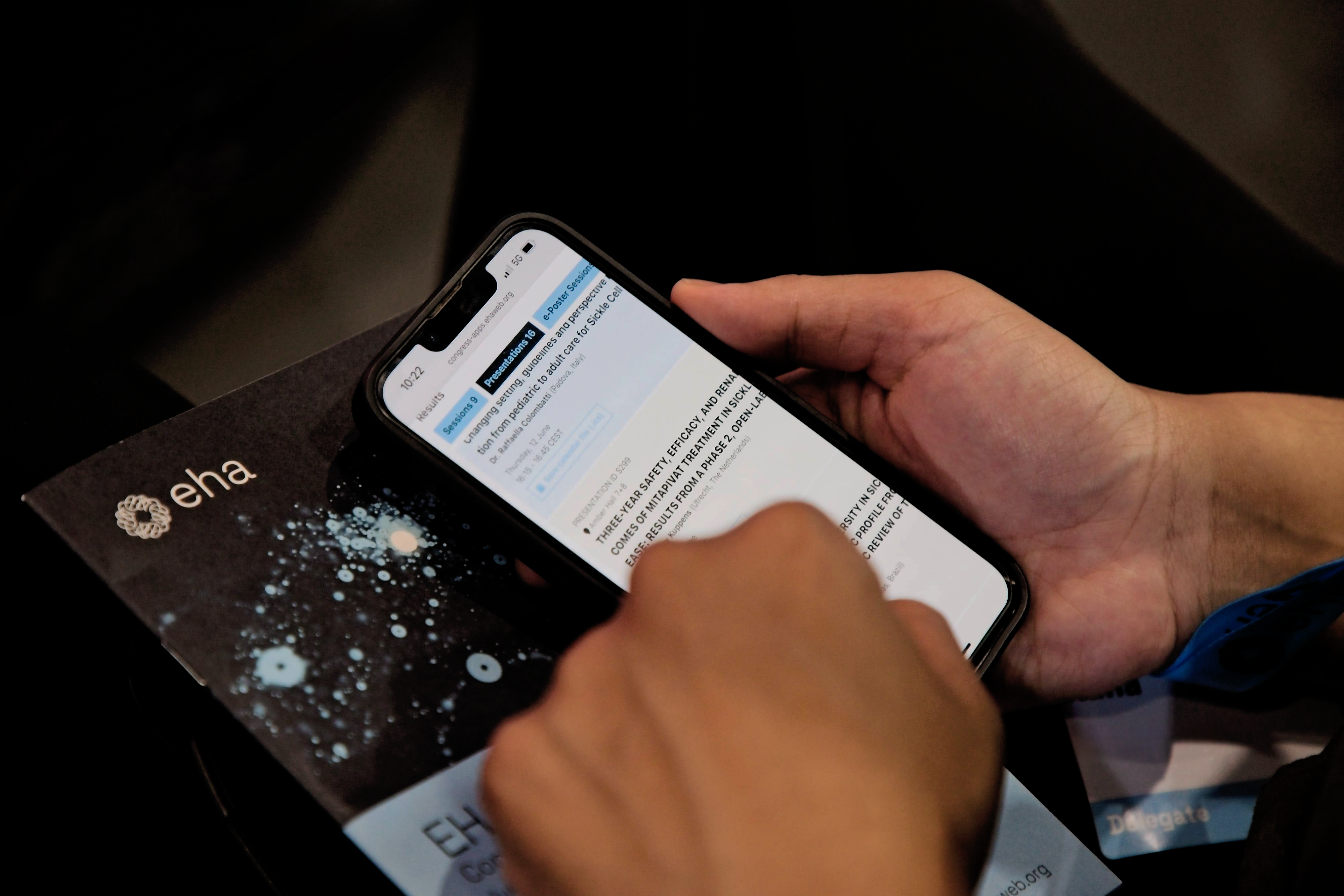 A person looking at the smartphone version of the EHA2025 program. Underneath their phone is a copy of the printed program.