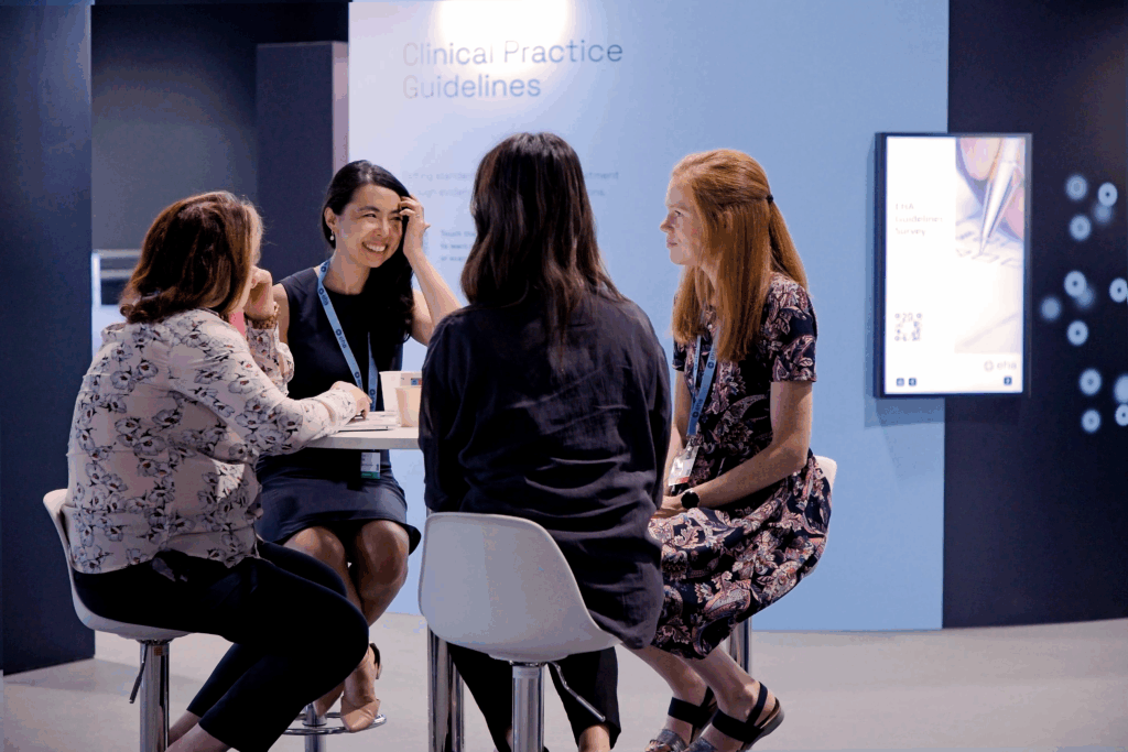 Four delegates sitting at a small table. Behind them is a screen and a sign that says 'Clinical Practice Guidelines.'