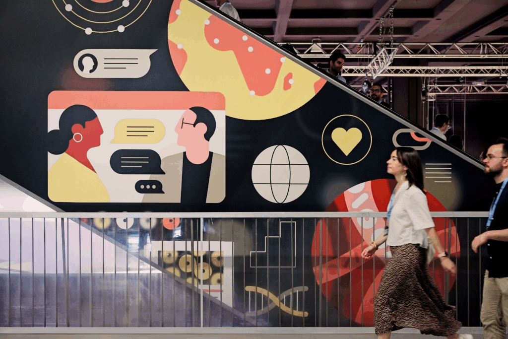 Two EHA2025 delegates walking past a large EHA illustration.
